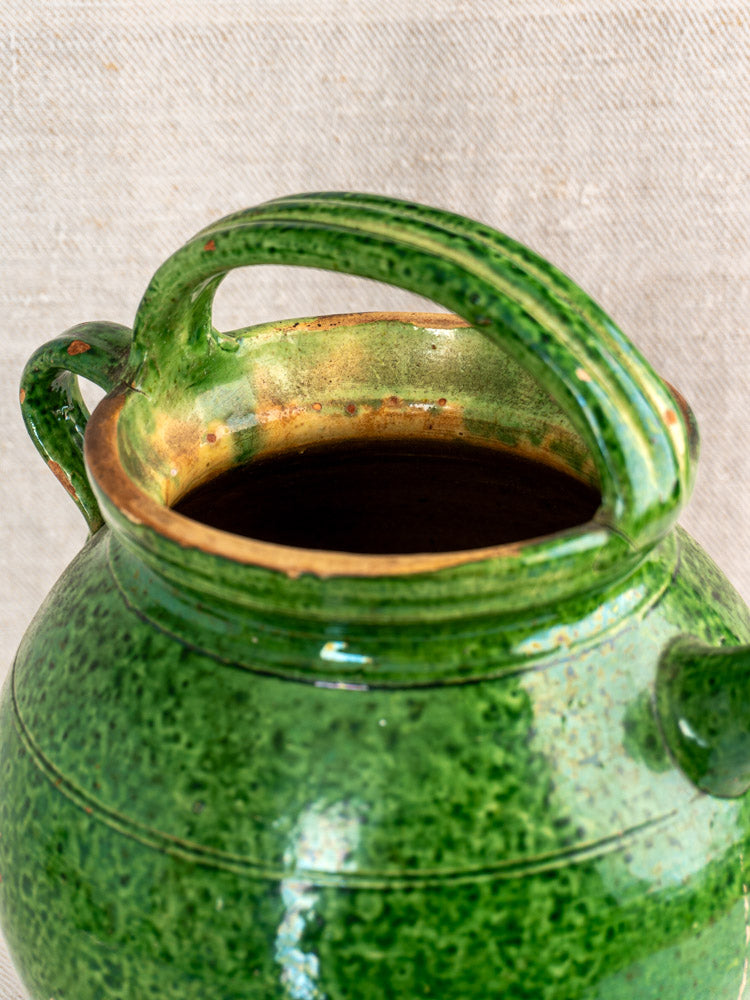 Antique French green glazed cruche orjol, early 20th-century Languedoc water jug on neutral fabric background.