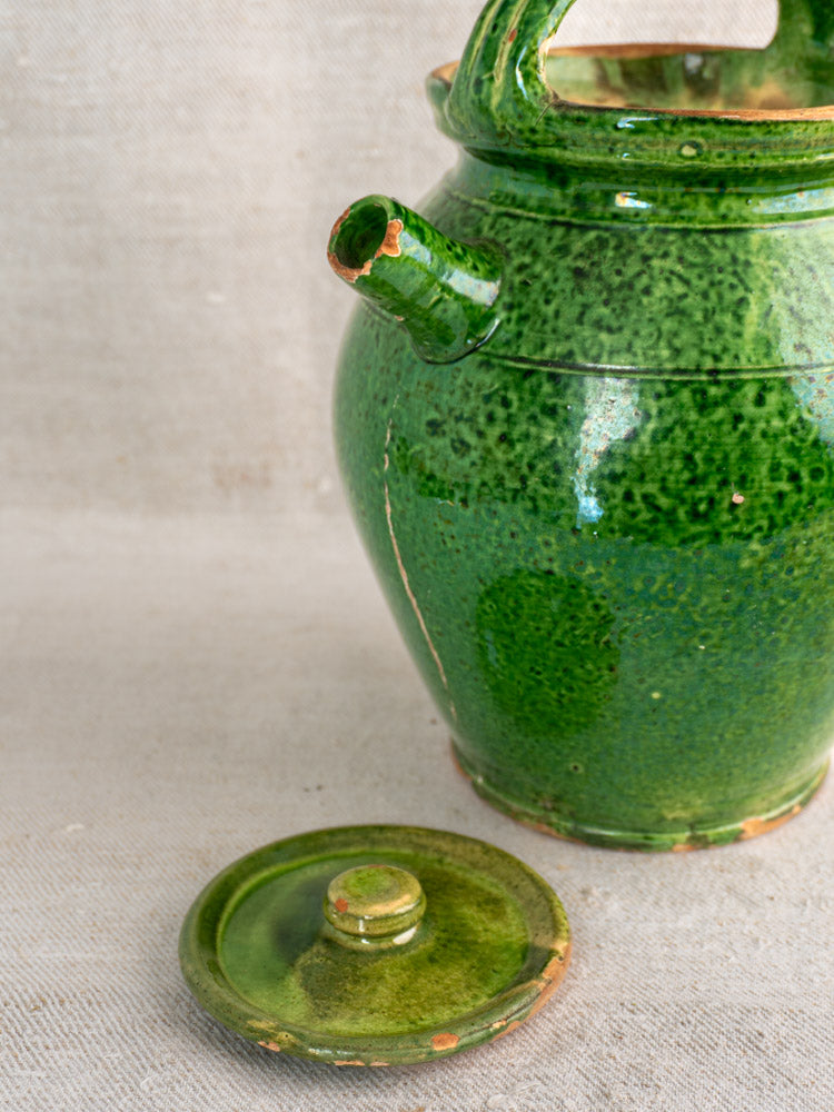 Antique French green glazed cruche Orjol Languedoc water jug with lid, spout, handle; worn glaze on beige textured surface.