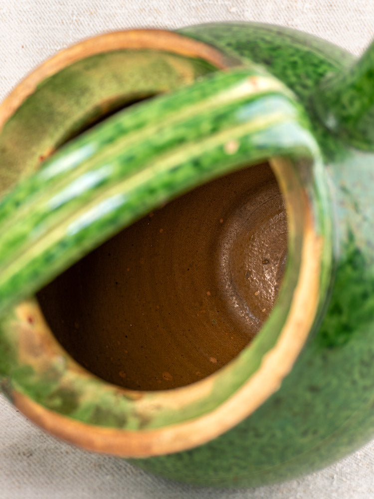 Antique French green glazed cruche orjol, glossy handled water jug with brown interior on light fabric.