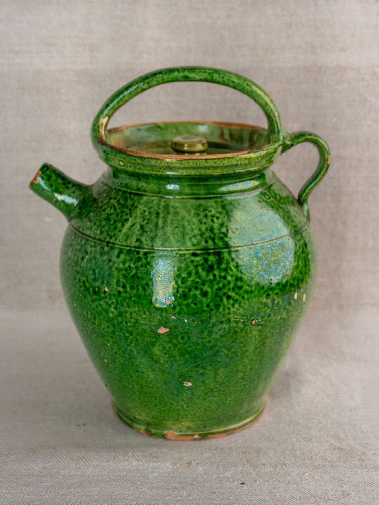 Antique French green glazed cruche orjol, early 20th-century Languedoc jug with chips on neutral textured background.