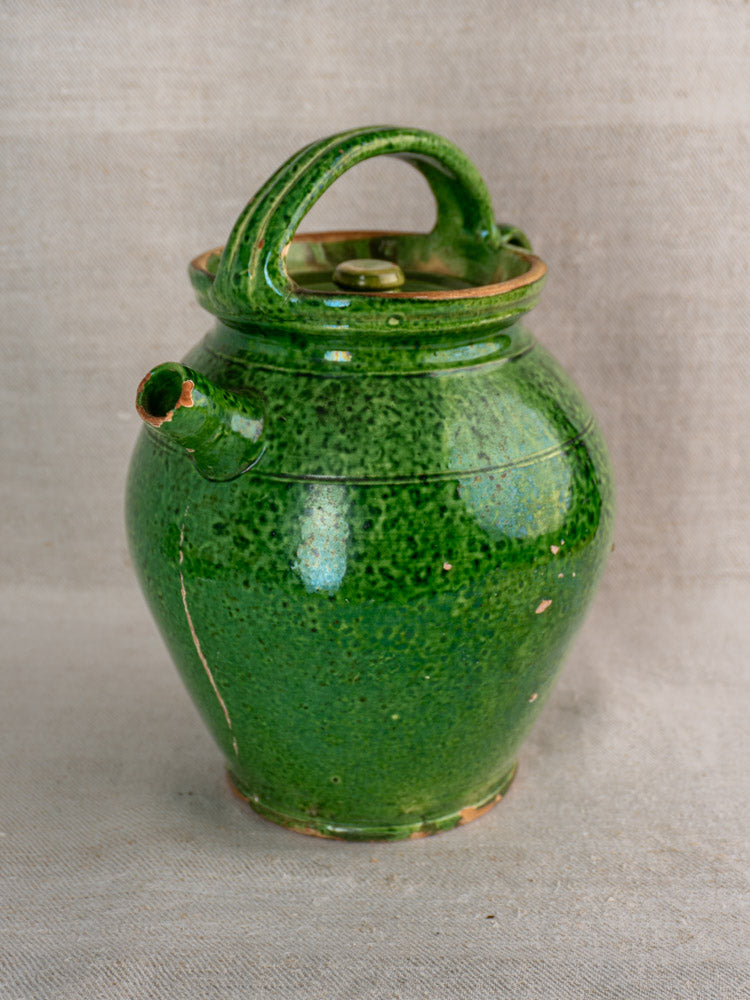 Antique French green glazed cruche Orjol Languedoc water jug with lid on neutral textured fabric background.