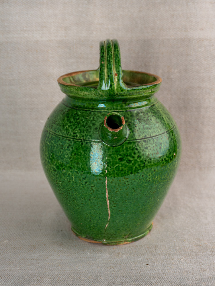 Antique French green glazed cruche orjol water jug, Languedoc, rounded body, side spout, visible cracks, neutral fabric backdrop.