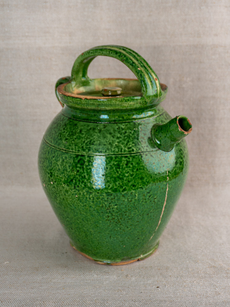 Antique French green glazed cruche Orjol Languedoc water jug with lid and handle on neutral fabric background.