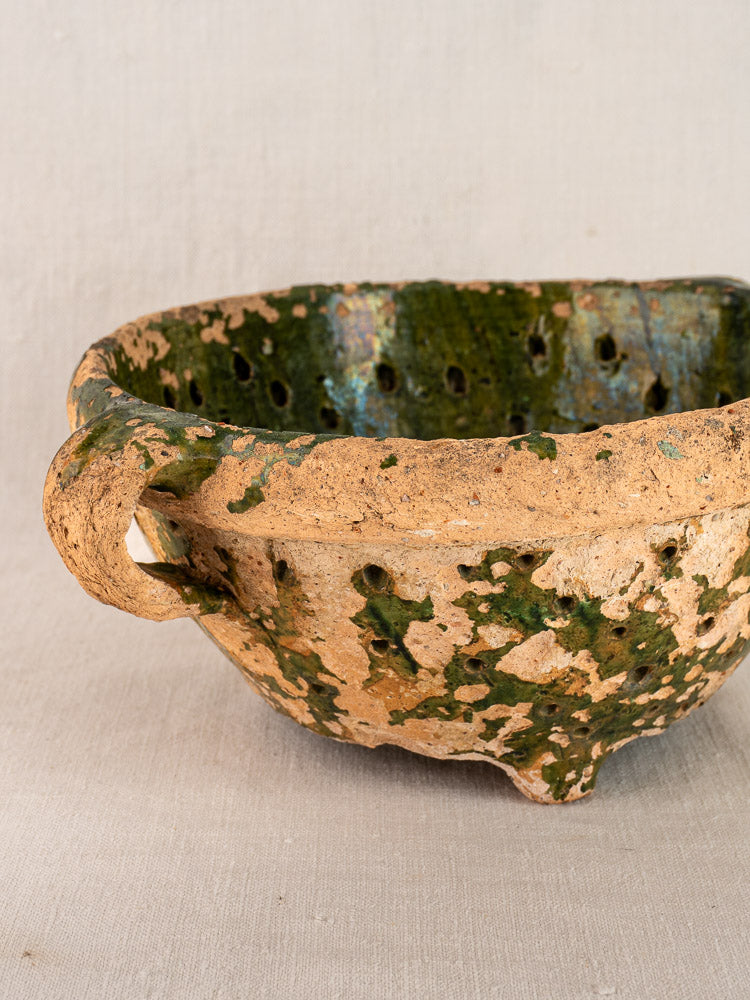 Antique French green glazed terracotta colander, late 18th century, handmade with single handle and three feet on neutral fabric.