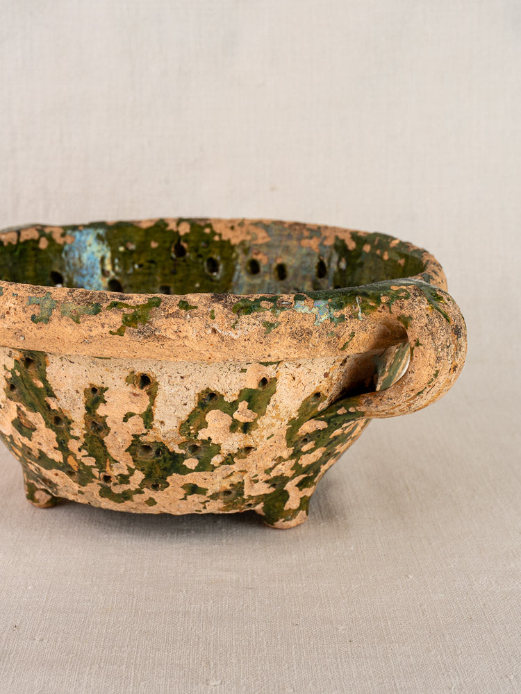 Antique French green glazed terracotta colander with handle and feet, late 18th century, on neutral fabric background.