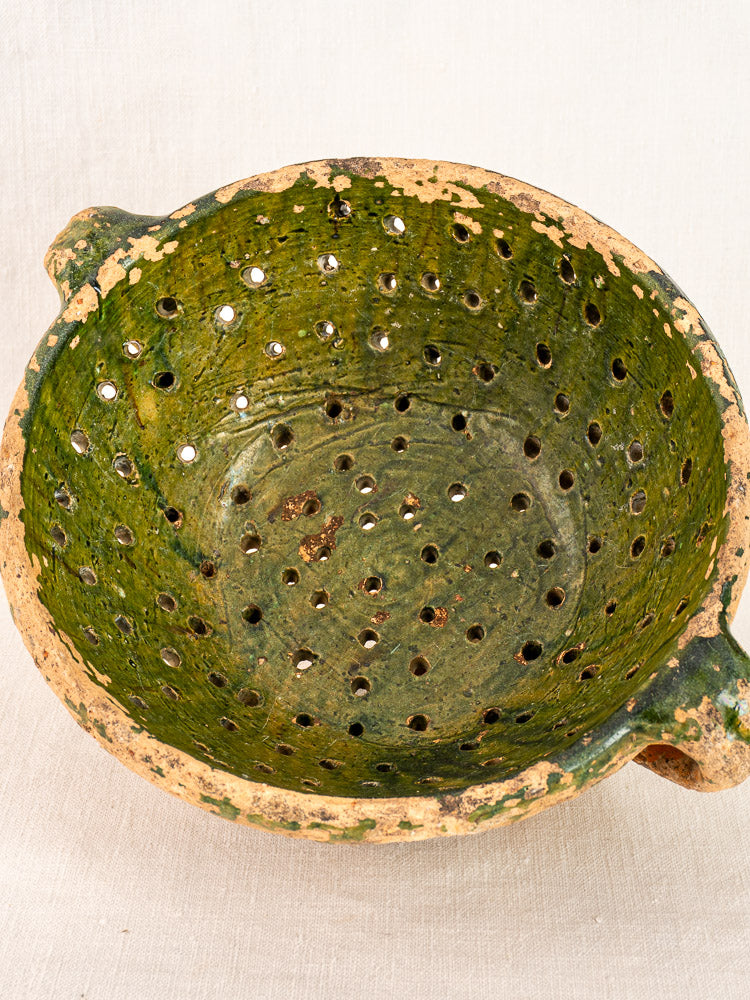 Late 18th-century French green glazed terracotta colander with two handles, worn edges, and perforated folk pottery design.