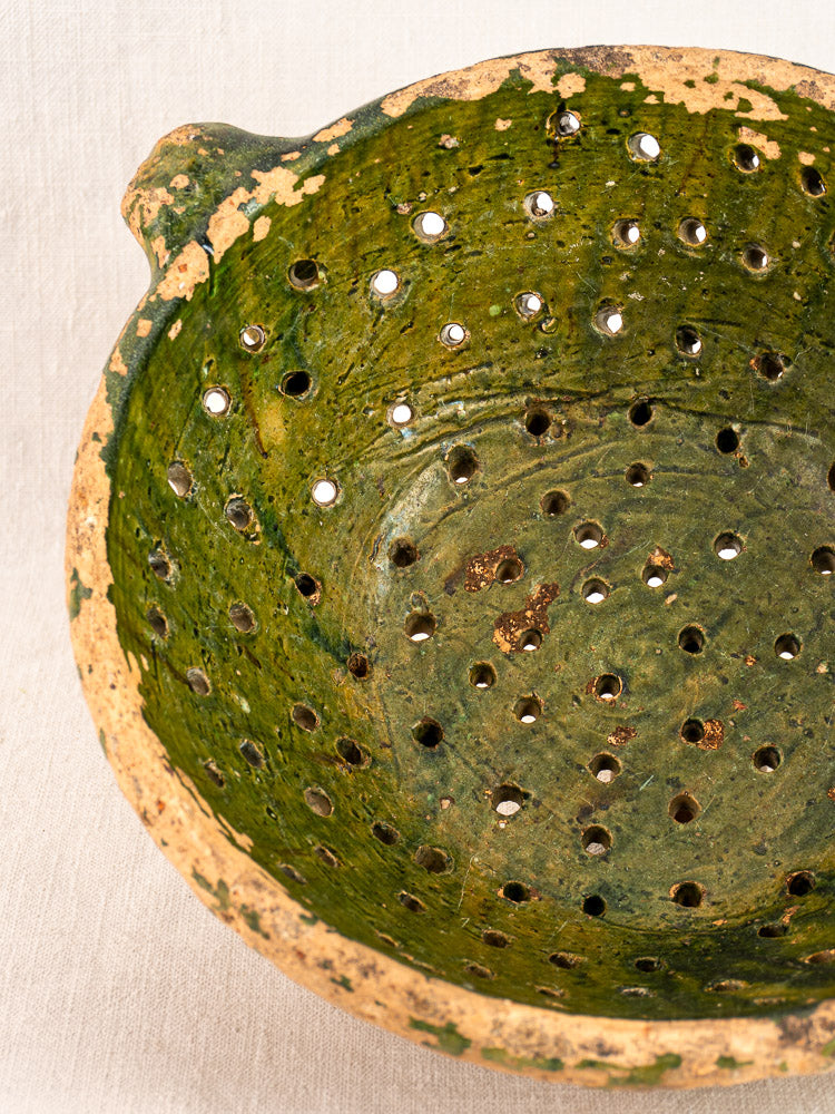 Antique French green glazed terracotta colander with twin handles, drainage holes, and worn edges showing rustic folk pottery style.