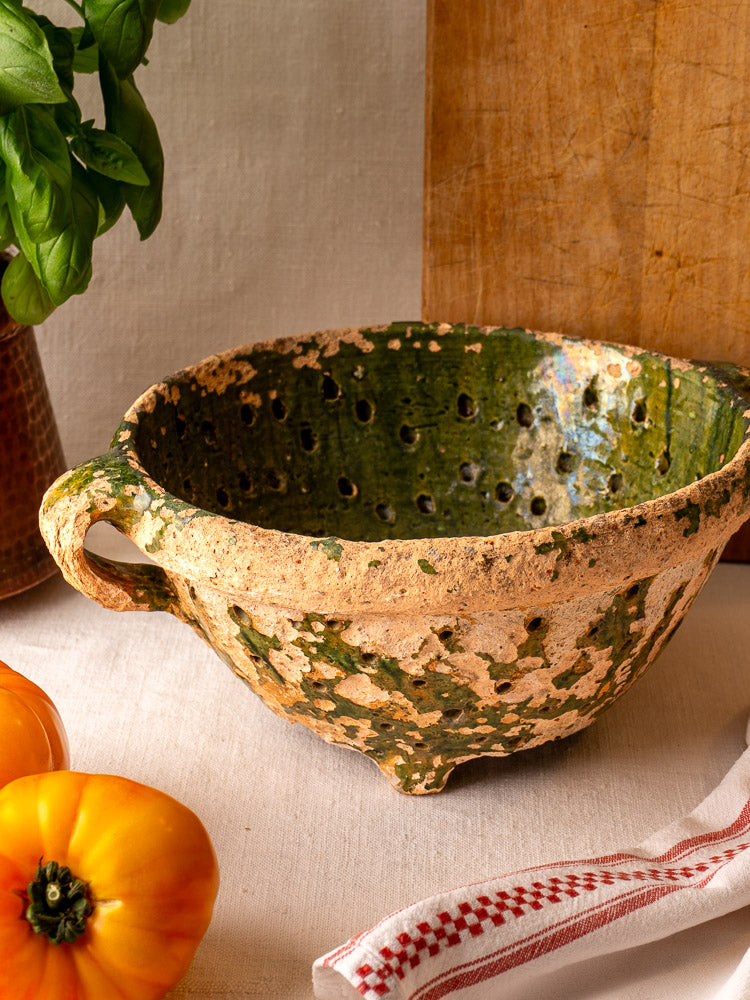 Antique French green-glazed terracotta colander, late 18th century, displayed on white linen with tomatoes and fresh basil.