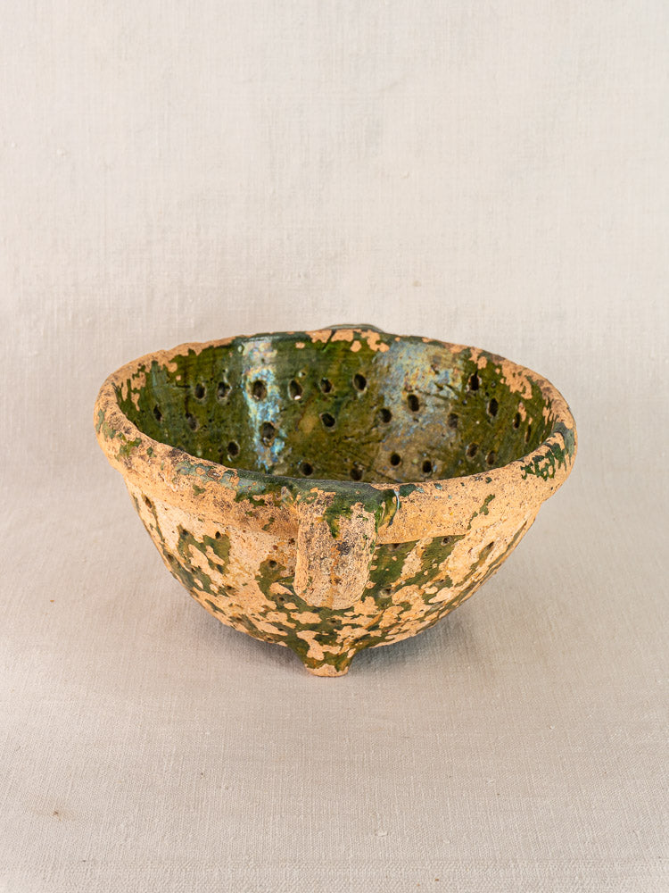 Late 18th-century French colander in green glazed terracotta with textured surface and perforations, set against beige background.