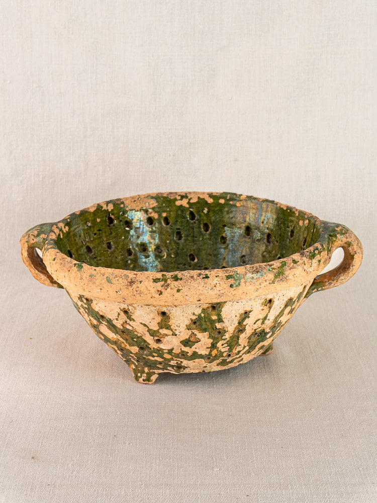 Antique French colander, late 18th century, with green glazed terracotta, twin handles, and drainage holes on neutral fabric.