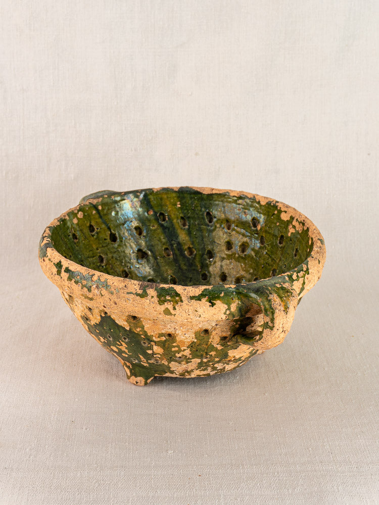 Late 18th century French green glazed terracotta colander with handle, brown clay accents, textured surface on neutral fabric.