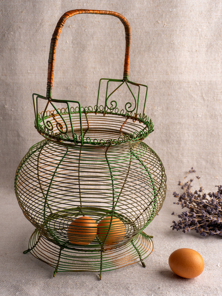 Antique French green wire egg basket with scroll rim, two brown eggs, beige fabric, and dried lavender bundle.