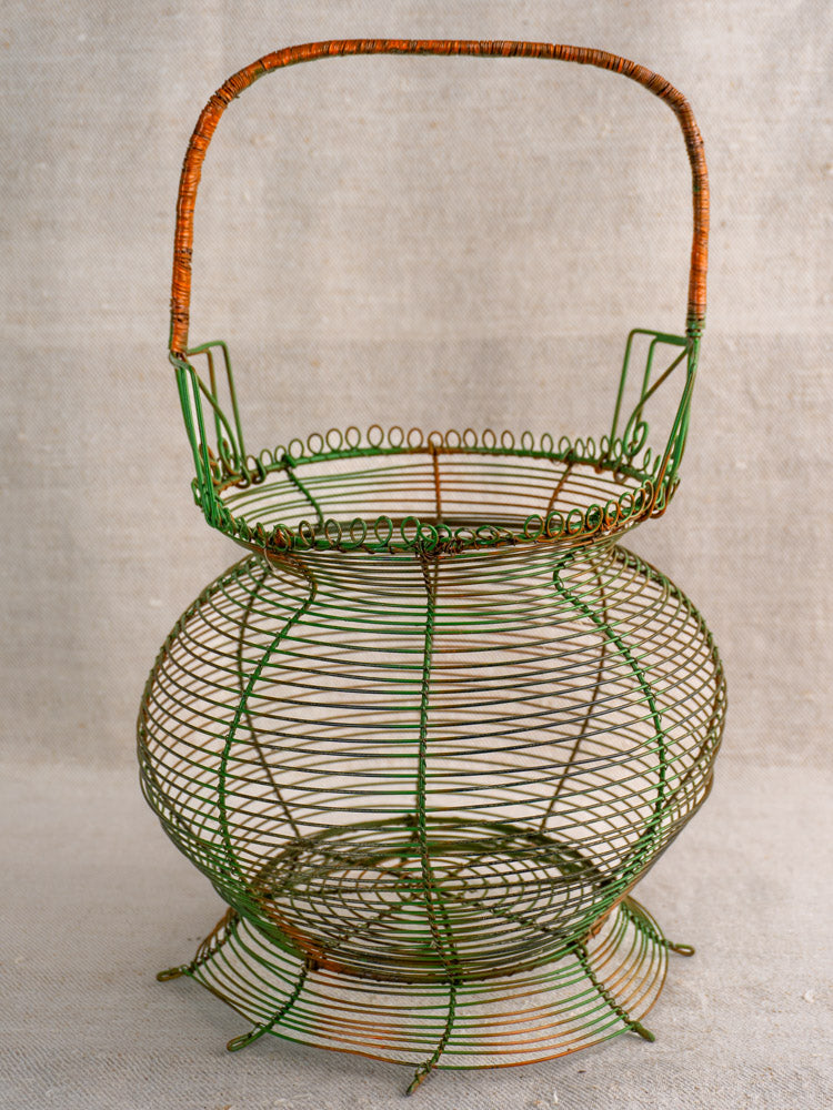 Antique French green wire egg basket with scroll rim and original paint on neutral textured fabric. Mid 20th century.