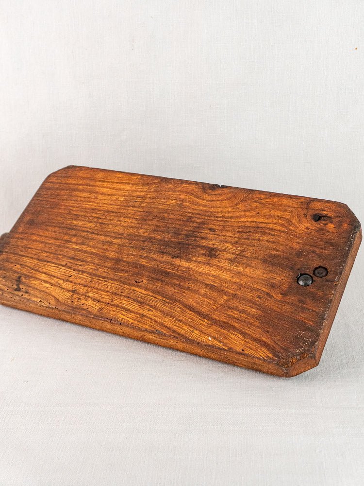 Antique French bread cutter with rounded edges and visible grain on a light fabric surface.