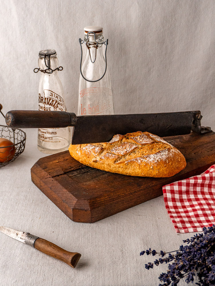 Antique French bread cutter with a long metal guillotine blade and wooden base on neutral background.