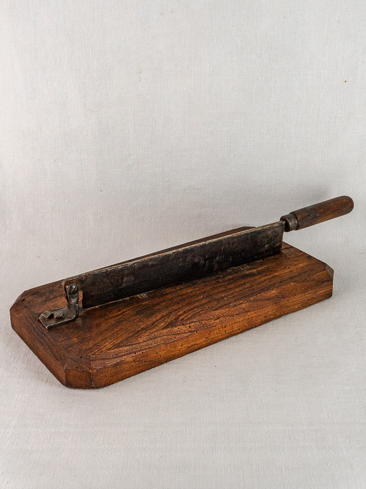 Antique French bread cutter with a long metal guillotine blade and wooden base on neutral background.