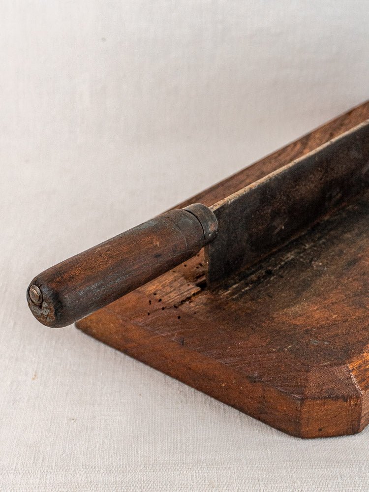 Antique French bread cutter with aged wood handle and rustic blade on vintage cutting board.