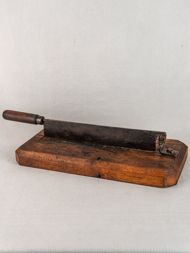 Antique French guillotine bread cutter with wooden base and handle, on light fabric background.