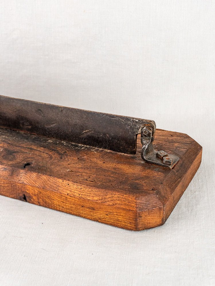 Antique French bread cutter with guillotine blade and metal hinge on wooden base, shown on light fabric.