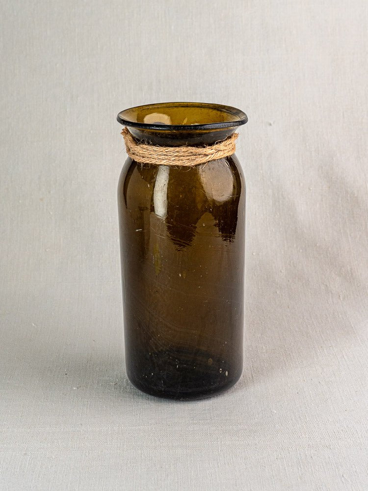 Antique French hand blown olive green glass bocal with twine, on light grey textured surface.