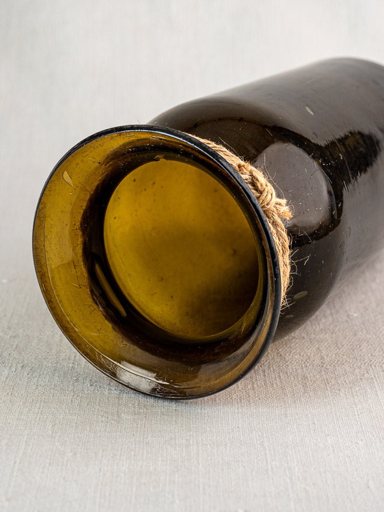 Olive green hand-blown glass French bocal with twine-wrapped neck on a light textured surface.