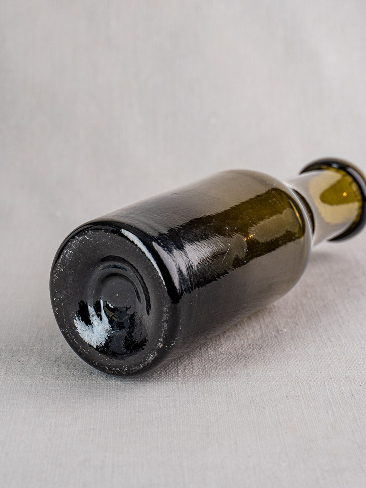 Antique French truffle jar in olive green hand-blown glass, base facing camera on gray surface.