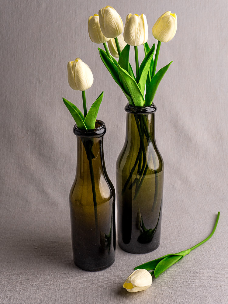 Pair of antique French olive green glass truffle jars with white tulips on gray fabric.