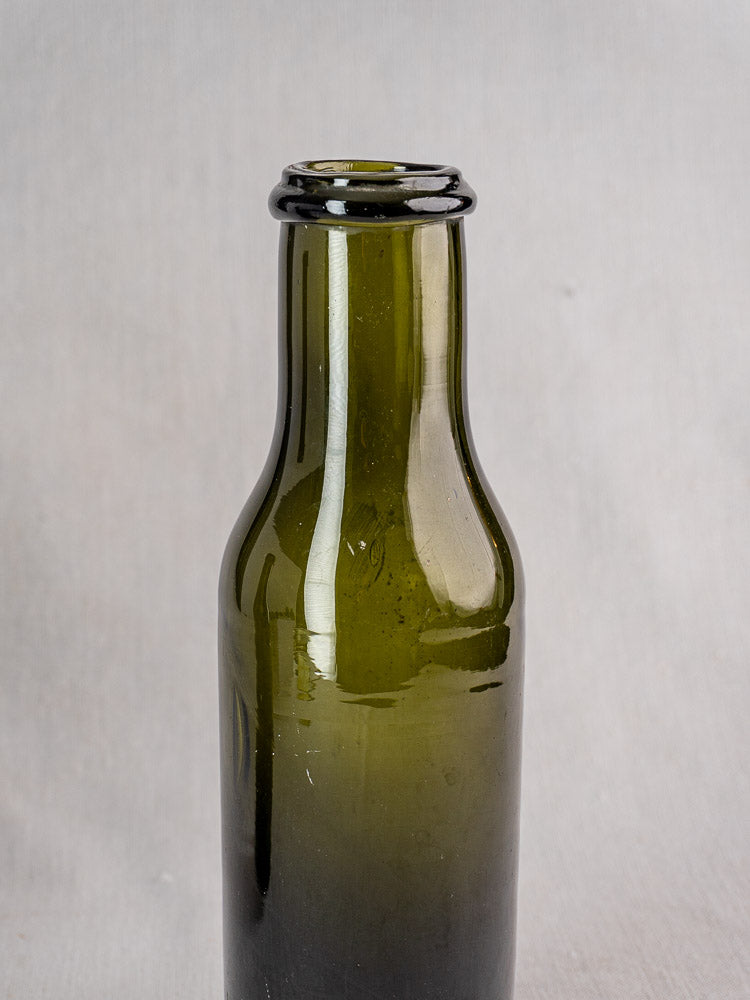 Antique French hand blown olive green glass truffle jar, upright on a light gray background.