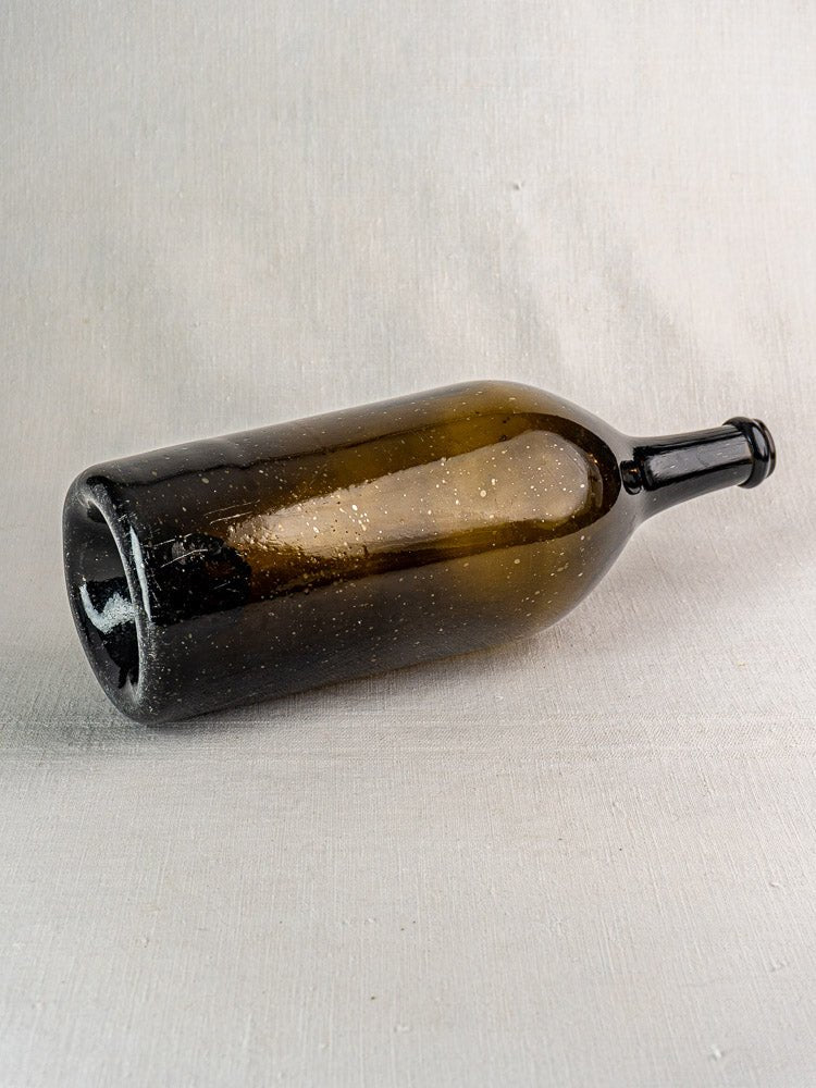 Large antique French hand-blown dark olive glass wine bottle with speckled surface and textured background.