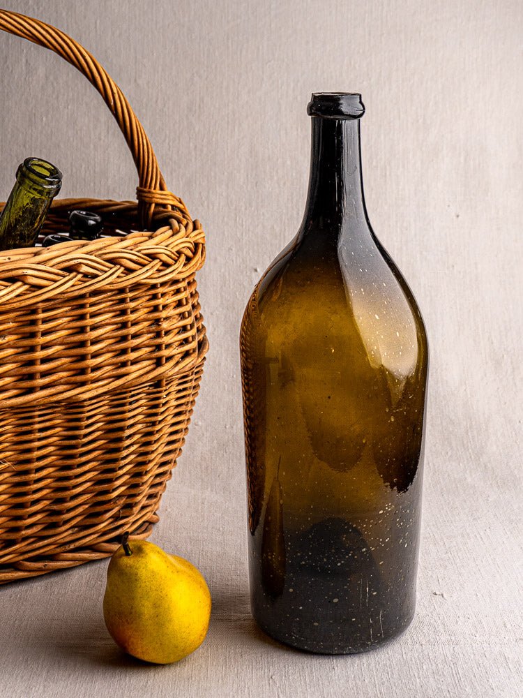 Large 19th-century French hand blown dark olive wine bottle with yellow pear and wicker bottle basket.