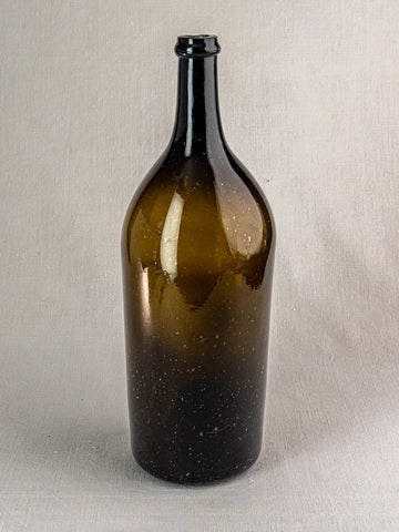 Large 19th-century French hand-blown wine bottle in dark olive glass with tall neck, on light textured surface.