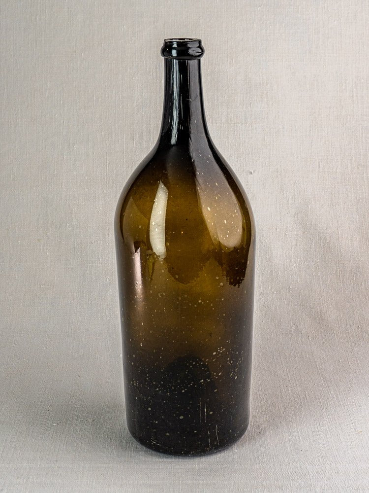Large 19th-century antique French hand blown wine bottle in dark olive glass on neutral textured surface.