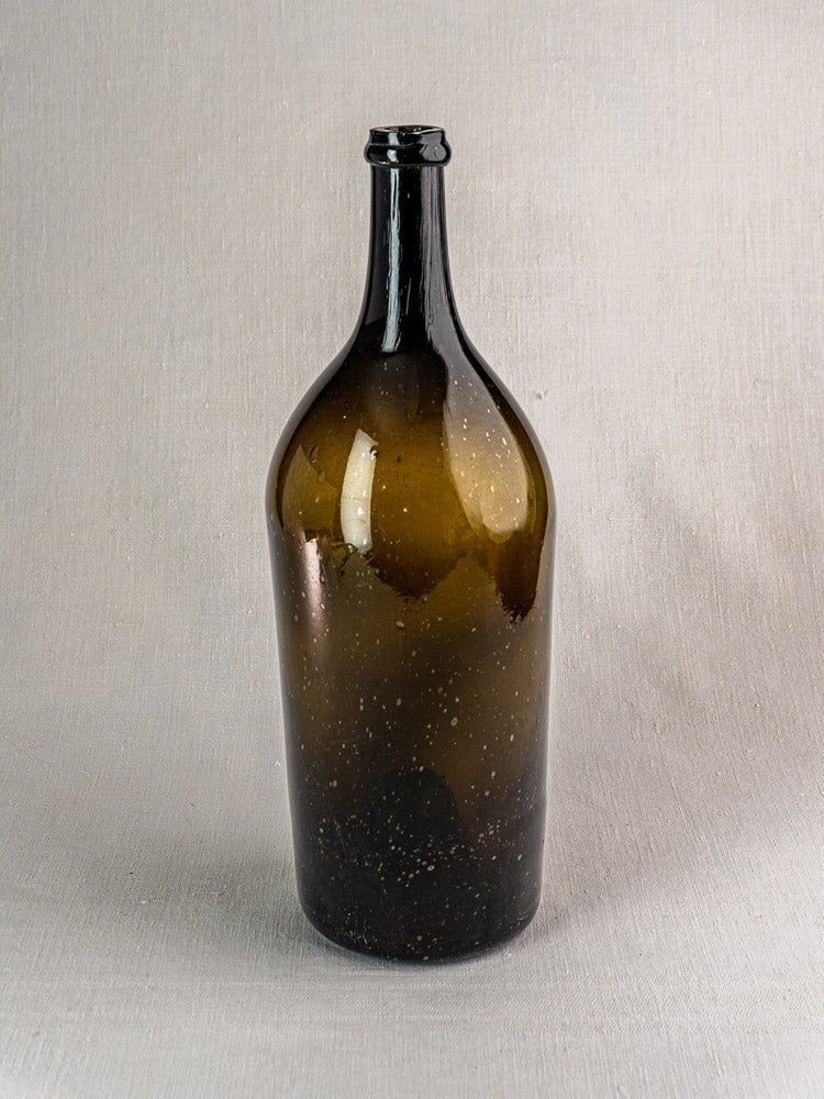 Large dark olive antique French hand-blown 19th-century wine bottle with narrow neck on gray textured surface.