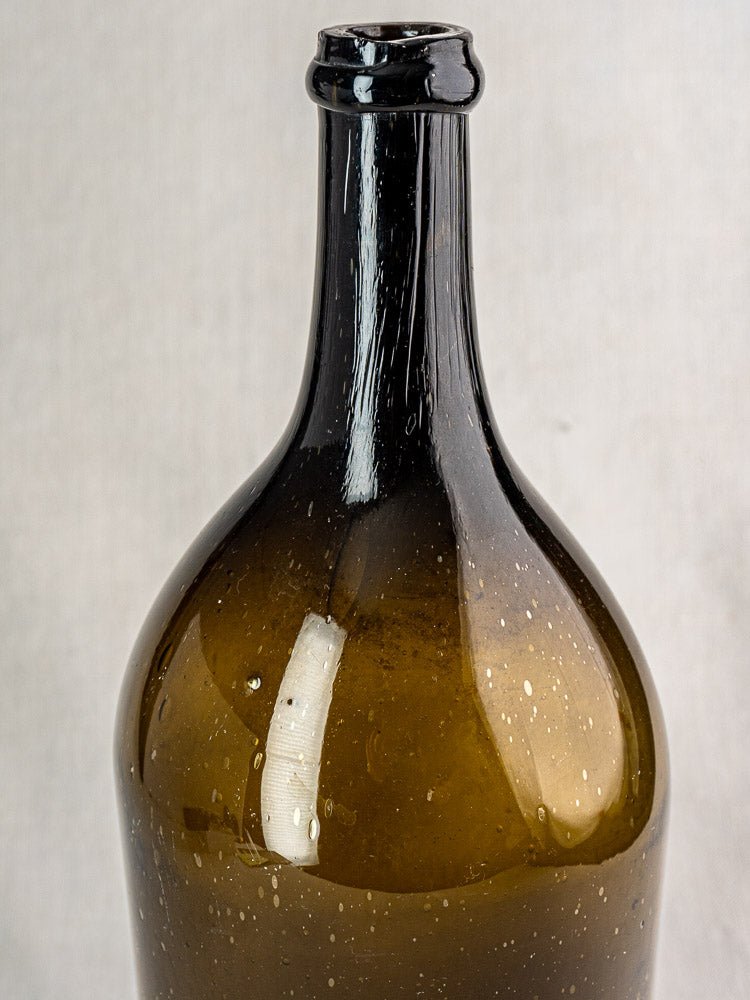 Large antique French hand blown wine bottle in dark olive glass with visible air bubbles.
