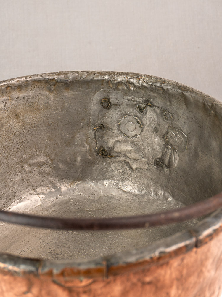 Antique French copper cauldron with tarnished patina, rough rim, and soldered repairs typical of farmhouse cookware.