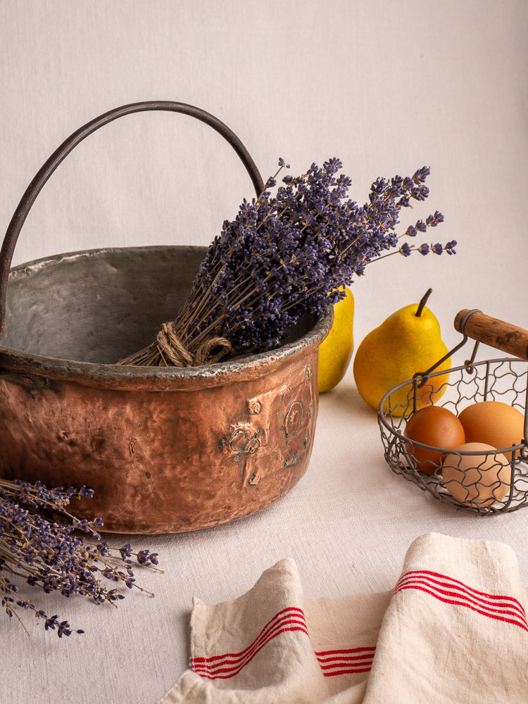 Antique French copper cauldron with repairs, rounded form, weathered patina, and handle on light gray background.