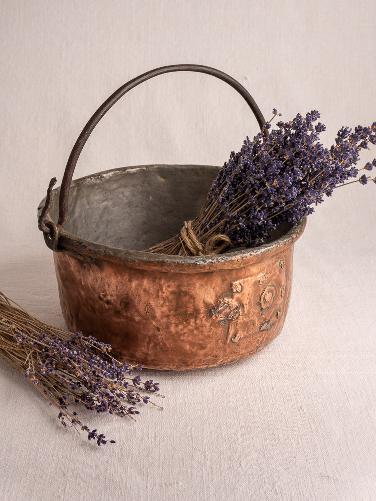 Antique French copper cauldron with dark handle, filled with dried lavender, another bundle resting on light fabric.
