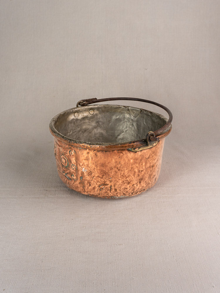Antique French copper cauldron with hammered finish, metal side handles, weathered patina on light surface.