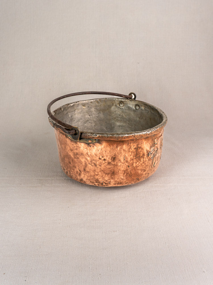 Antique French copper cauldron, 17th–18th century, with unique repairs and dark handle on light gray background.