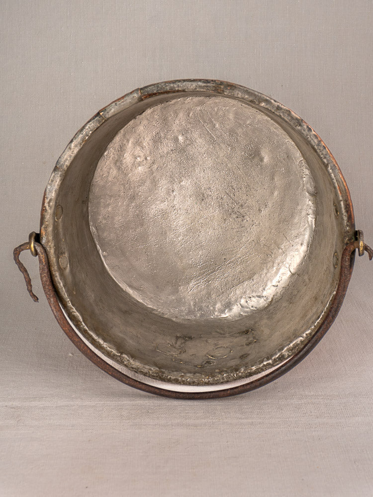 Antique French copper cauldron with round opening, worn interior, and side handles; unique repairs; plain light background.