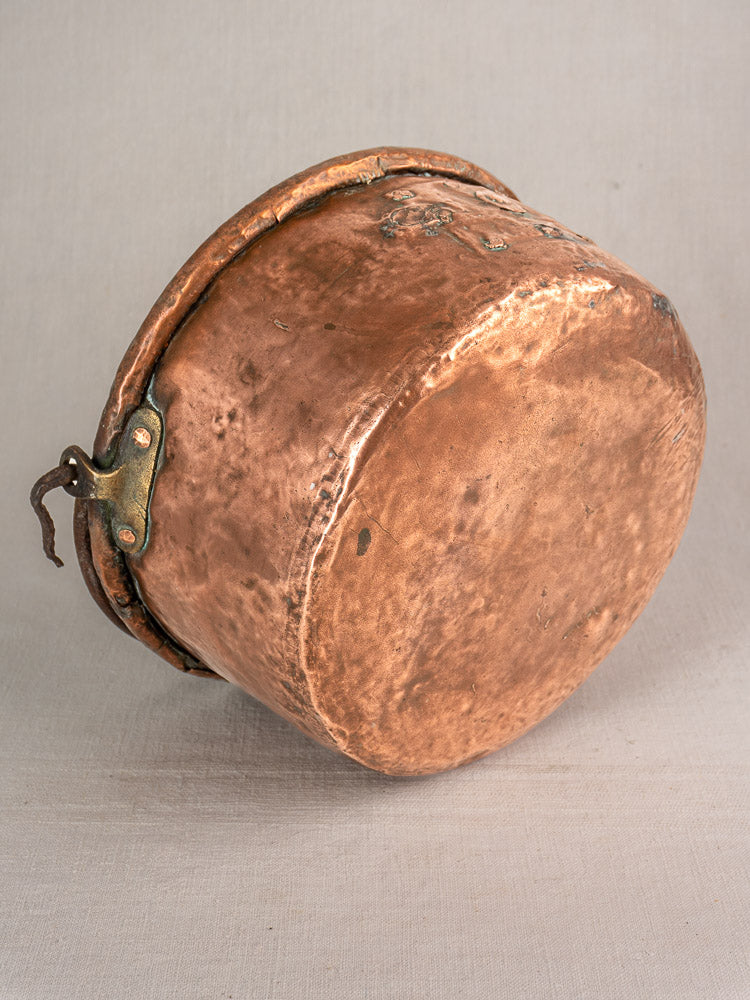 Large antique French copper cauldron, hand-hammered with repairs, weathered patina, riveted handle, and visible age-related wear.