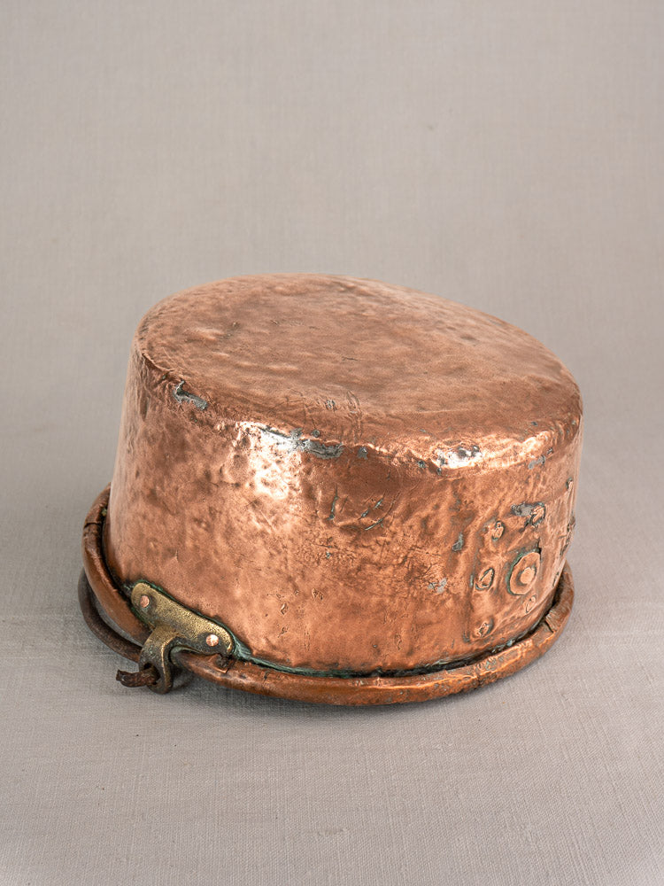 Antique French copper cauldron with hammered body, unique repairs, and thick metal band on neutral gray background.