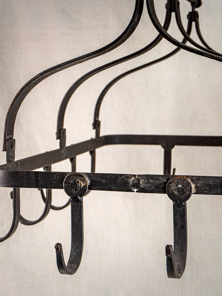 Antique French wrought iron hanging pot rack with curved hooks, shown on a neutral beige background.