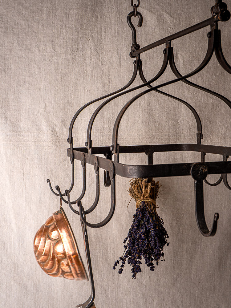 Antique French wrought iron hanging pot rack with copper pan and dried lavender on beige fabric.