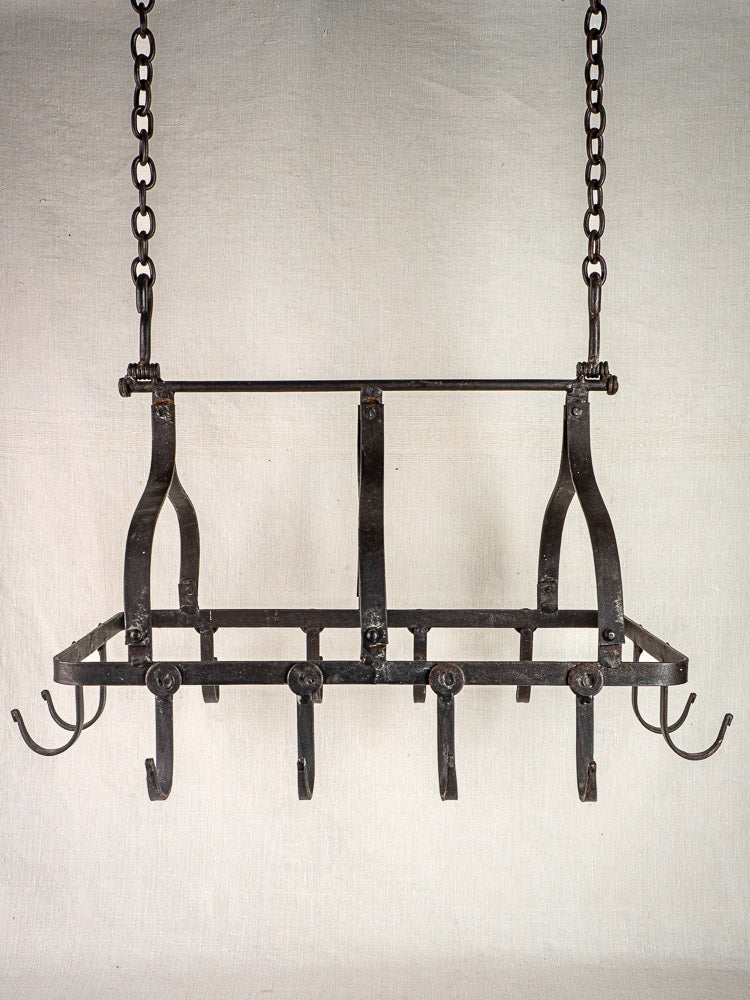 Rectangular antique French wrought iron pot rack with six hooks, two chains; plain background.