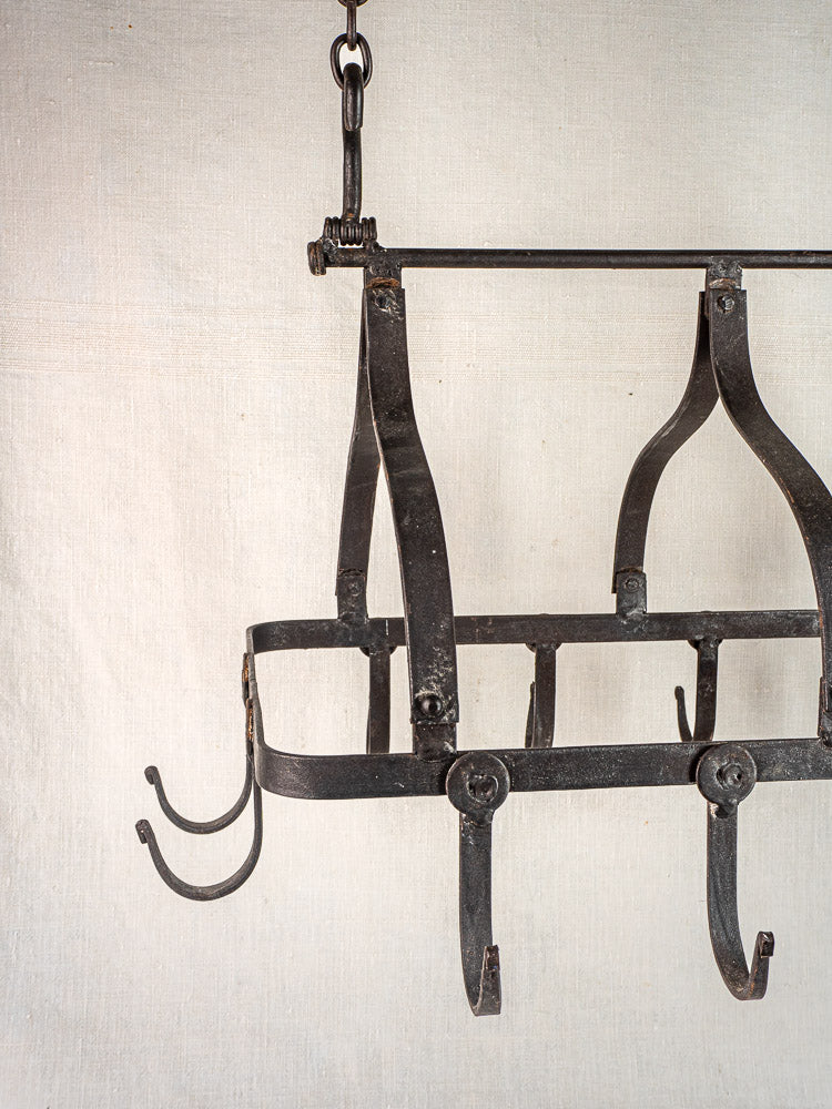 Antique French wrought iron hanging pot rack with curved hooks and chain, rustic kitchen accent.