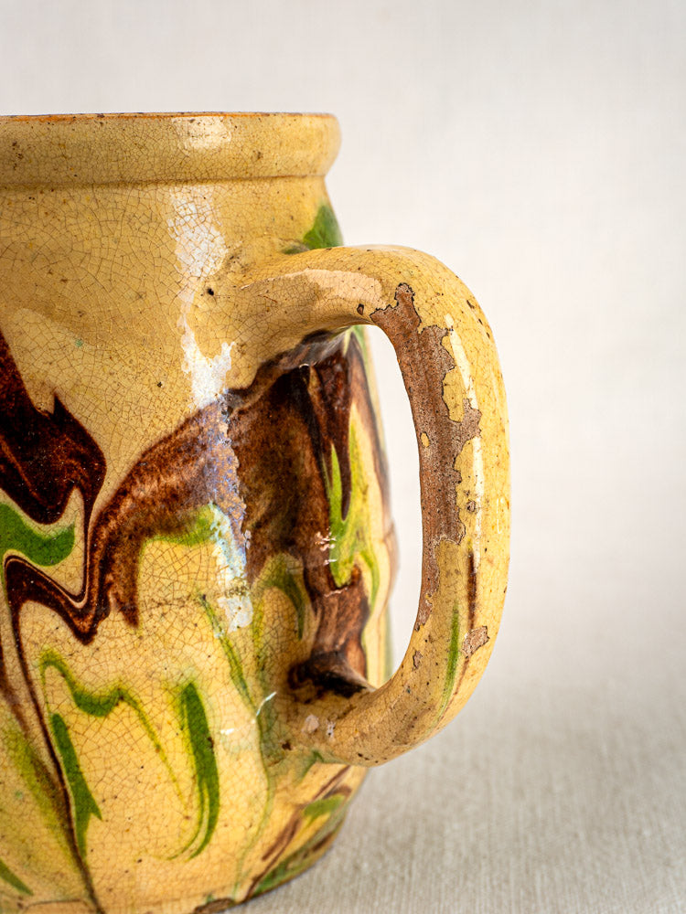 Antique French jaspé pitcher with marbled yellow glaze, green and brown patterns, and characterful cracks.