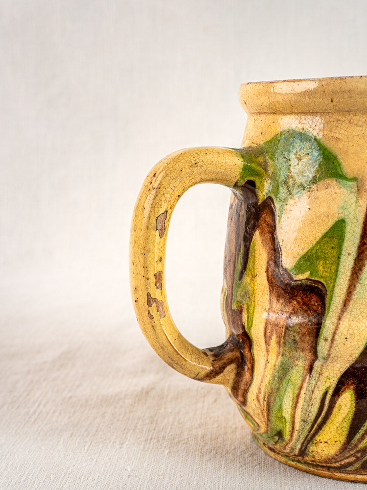 Antique French Jaspé pitcher with yellow, brown, and green marbled glaze on light fabric background.