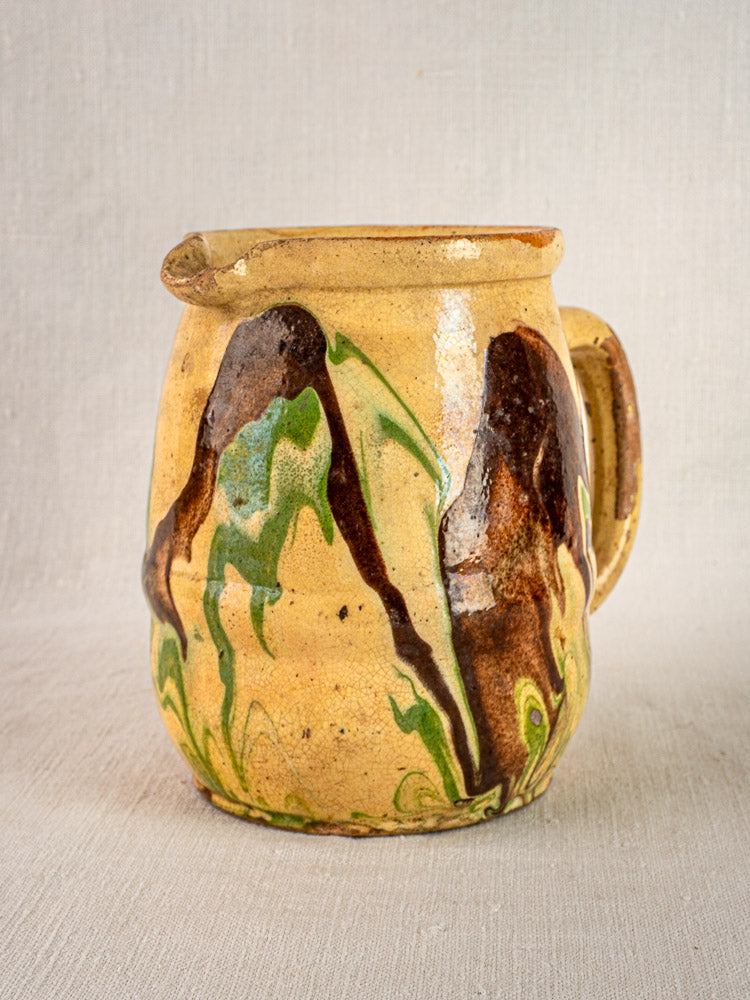 Antique French ceramic pitcher with handle, yellowish base, and brown, green, and black marbled glaze.
