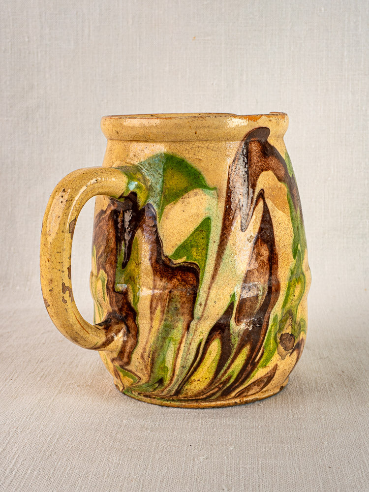 Antique French Jaspé pitcher with Savoie marbled green and brown glaze, on neutral fabric background.